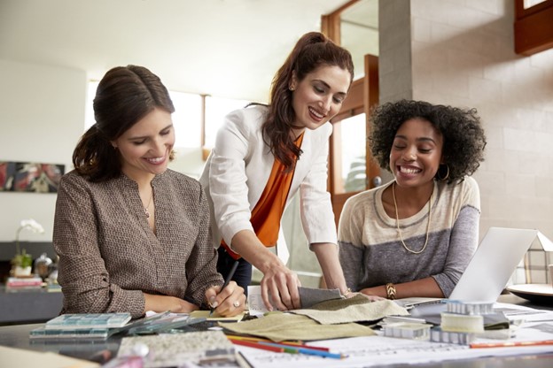Three women working together on website strategy for a small business, with a laptop and creative materials.